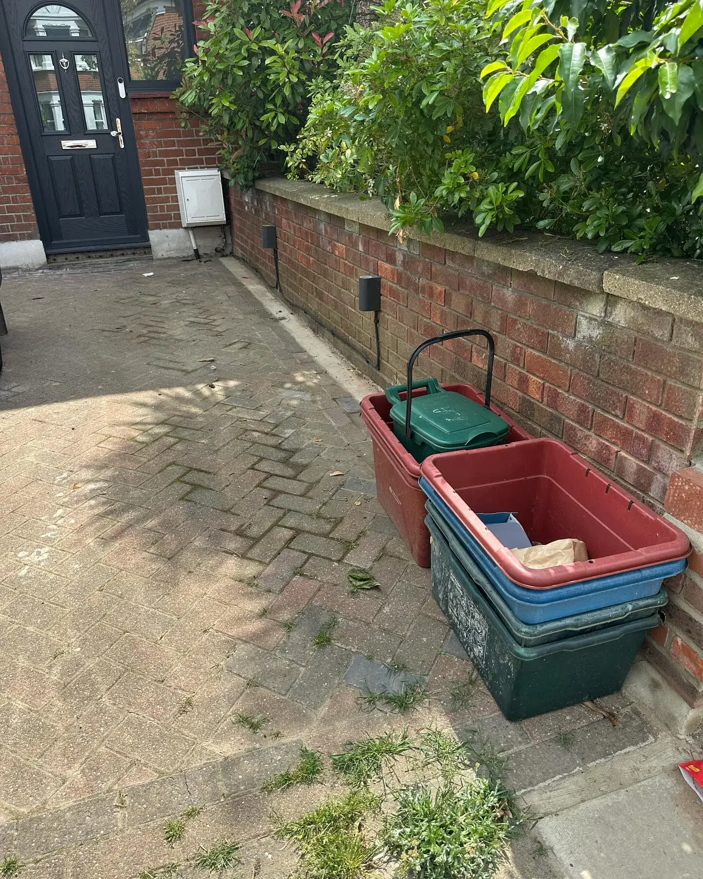 Garden waste bins filled and lined up by a front wall